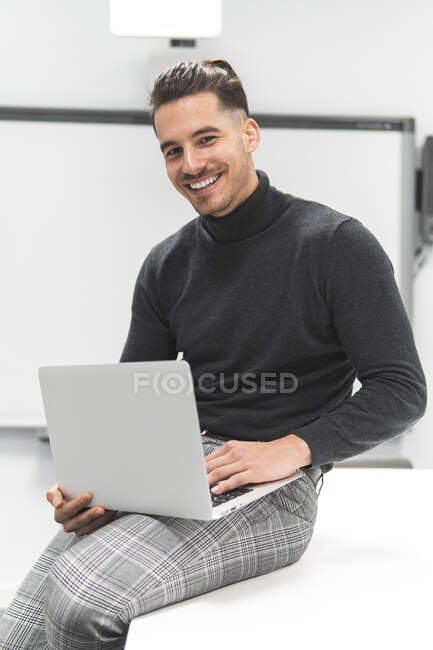 Молодий бізнесмен з ноутбуком сидить на столі в настільній кімнаті в офісі — стокове фото