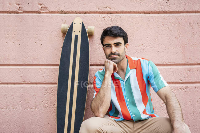 Schöner Mann mit der Hand am Kinn am Longboard sitzend — Stockfoto