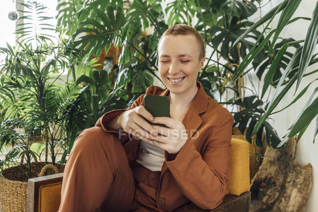 Sorridente giovane donna d'affari utilizzando smart phone in ufficio verde — Foto stock