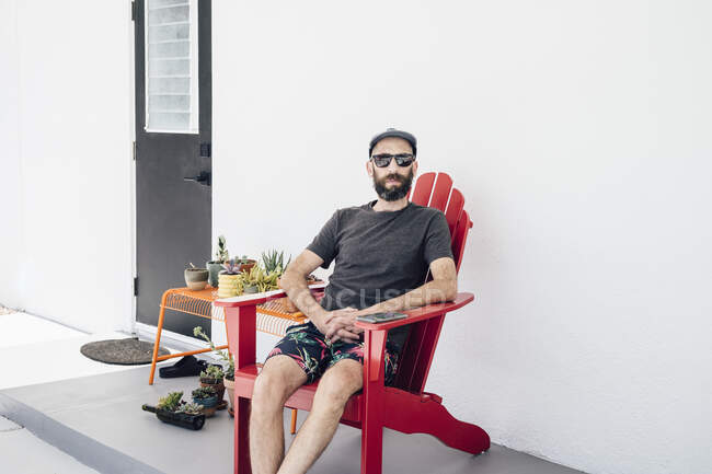 Hombre barbudo con gafas de sol sentado en la silla en el patio - foto de stock