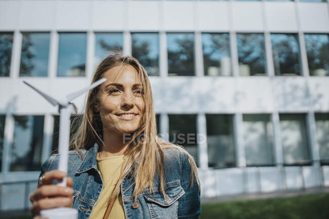 Женщина в джинсовой куртке держит модель ветряной турбины перед современным офисным зданием — стоковое фото