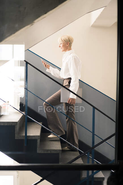 Femme entrepreneur utilisant un téléphone intelligent tout en marchant sur l'escalier dans l'appartement loft — Photo de stock