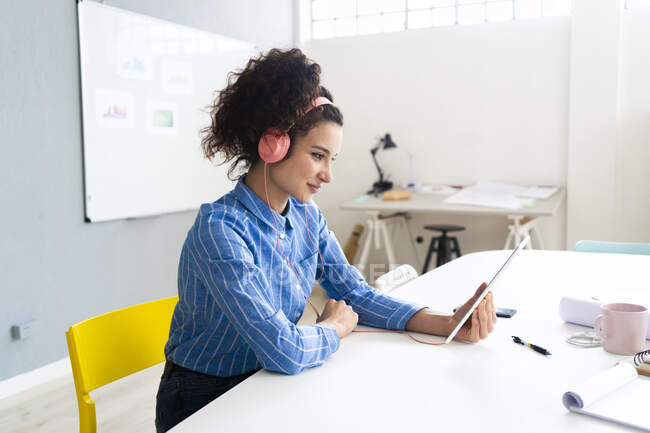 Жіночий підприємець з навушниками за допомогою цифрового планшета під час роботи в креативному офісі. — стокове фото
