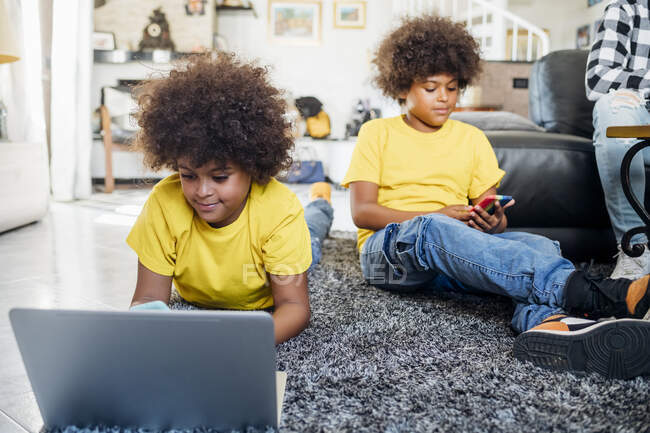Hermanos gemelos que utilizan tecnologías inalámbricas en casa - foto de stock