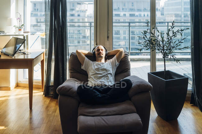 Young man with hands behind head relaxing on reclining chair at home — Stock Photo