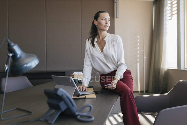 Female professional with laptop and mobile phone sitting at desk — Stock Photo