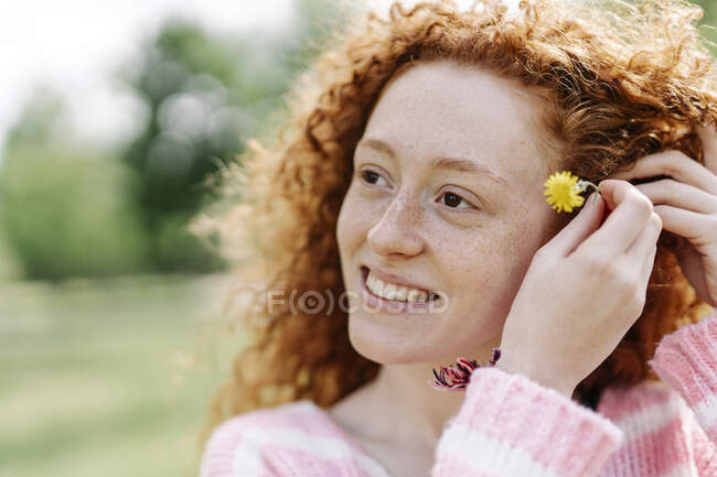 Bella donna rossa sorridente che indossa fiore mentre distoglie lo sguardo — Foto stock