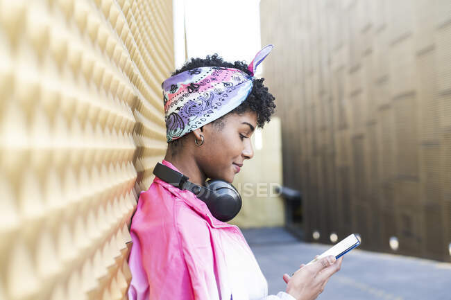 Woman using smart phone wearing bandana by wall — Stock Photo