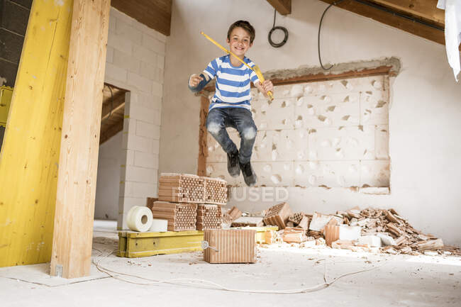 Boy with tape measure jumping at loft apartment during renovation — Stock Photo
