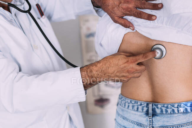 Male doctor checking female patient through stethoscope at clinic — Stock Photo