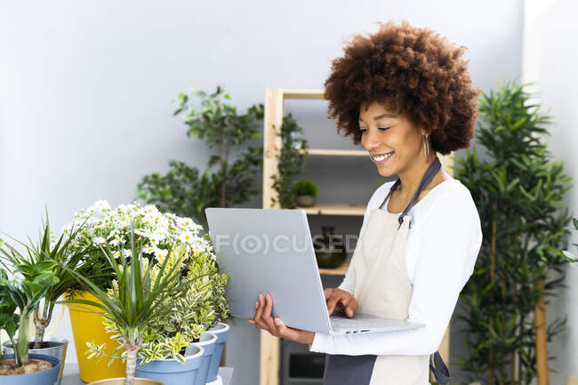 Fiorista sorridente utilizzando il computer portatile mentre in piedi vicino a piante in negozio — Foto stock