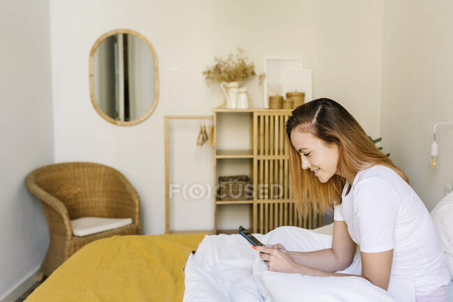 Donna dai capelli rossi che utilizza il telefono cellulare a casa — Foto stock