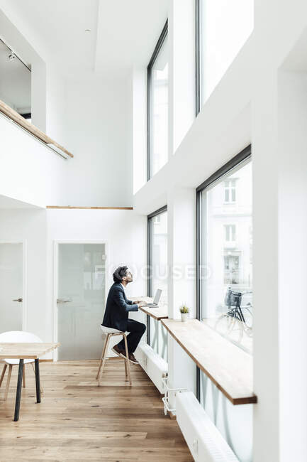 Männlicher Unternehmer sitzt mit Laptop im Büro und schaut durchs Fenster — Stockfoto