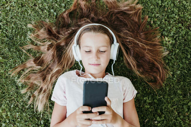 Ragazza che indossa cuffie ascoltare musica mentre sdraiato sull'erba — Foto stock