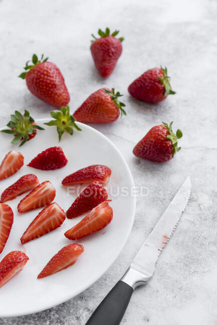 Кухонный нож и тарелка со свежей клубникой лежат на белом мраморе — стоковое фото