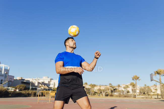 Homme mûr jouant avec le ballon de football sur le terrain de sport pendant la journée ensoleillée — Photo de stock