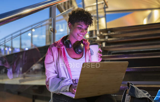 Посмішка молодої жінки з навушниками за допомогою ноутбука на кроках. — стокове фото