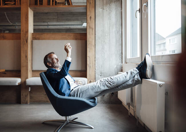 Uomo d'affari guardando roccia di legno mentre seduto sulla sedia in ufficio — Foto stock