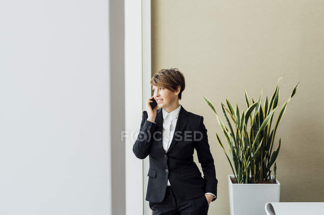 Smiling female business professional talking on smart phone while looking away — Stock Photo