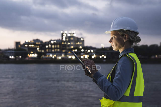 Female professional in protective workwear using digital tablet at dusk — Stock Photo
