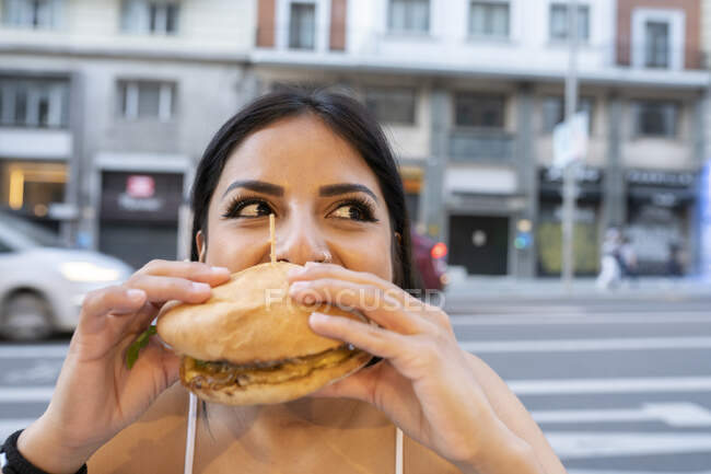 Giovane donna mangiare hamburger al caffè marciapiede durante il crepuscolo — Foto stock