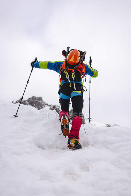 Trekker climbing snowcapped mountain with crampons and hiking poles — Stock Photo