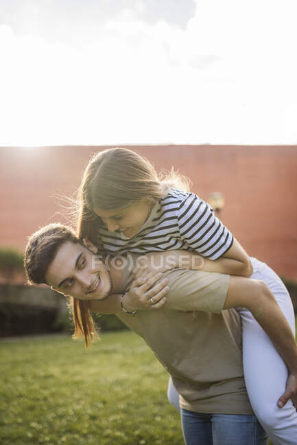 Boyfriend piggybacking girlfriend at lawn on sunny day — love, sunlight -  Stock Photo | #495973866