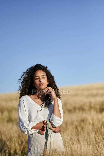 Giovane donna riflessiva con i capelli ricci in piedi nel campo di grano — Foto stock