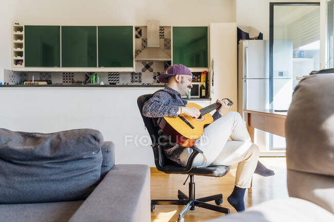Man playing guitar on chair at home — Stock Photo