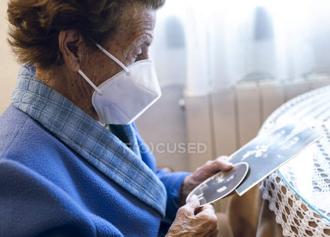 Seniorin mit Schutzmaske betrachtet altes Foto zu Hause — Stockfoto