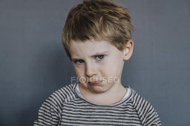 Menino inocente fazendo rosto no fundo cinza — Fotografia de Stock