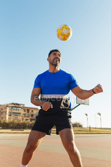 Homme en tenue de sport se dirigeant ballon de football sur le terrain — Photo de stock