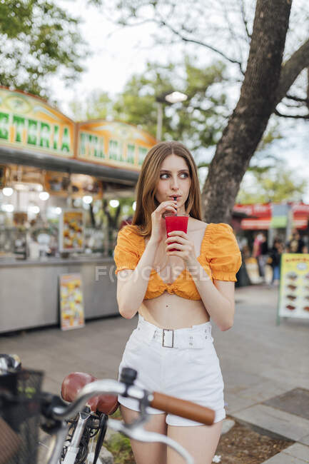 Donna che distoglie lo sguardo mentre beve succo sulla strada — Foto stock