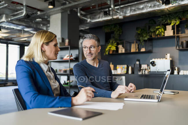 Male entrepreneur discussing with female professional while sitting with laptop in creative office — Stock Photo