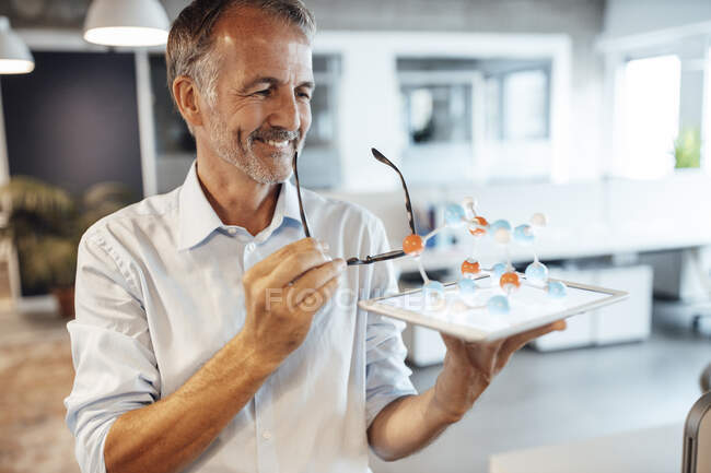 Бизнесмен с цифровыми таблетками и молекулярной моделью в офисе — стоковое фото