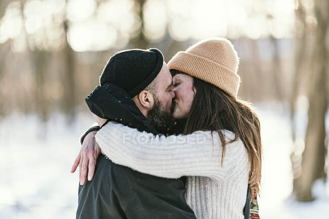 Couple adulte moyen en vêtements chauds s'embrassant dans la forêt — Photo de stock