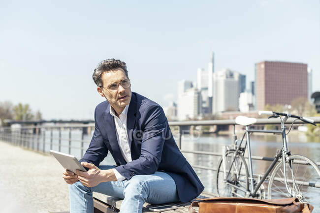 Задумчивый бизнесмен с цифровым планшетом сидит в солнечный день — стоковое фото