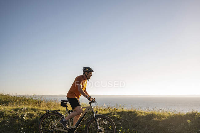 Desportista maduro andar de bicicleta elétrica por plantas verdes — Fotografia de Stock