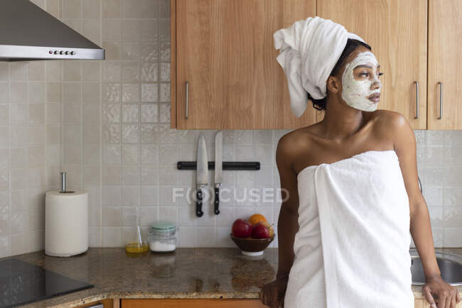 Mujer joven con toalla mirando hacia otro lado mientras está de pie en la cocina - foto de stock