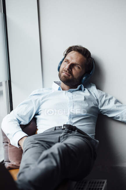Businessman with headphones looking away while resting in office — Stock Photo