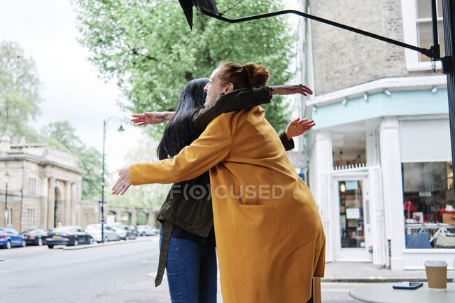 Female friends hugging at sidewalk cafe — Stock Photo
