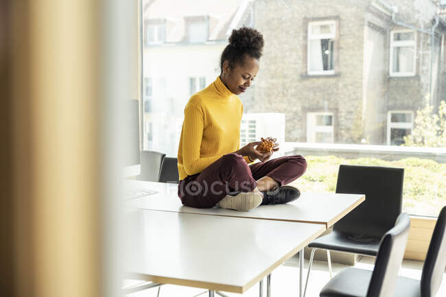 Femme d'affaires jouant avec puzzle cube tout en étant assis jambes croisées sur le bureau au bureau — Photo de stock