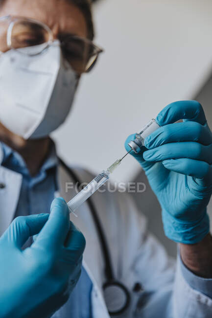 Medico generico di sesso maschile che riempie la siringa con il vaccino COVID-19 mentre si trova in clinica — Foto stock