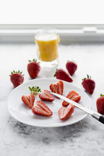Verre de jus d'orange, couteau de cuisine et assiette aux fraises fraîches couchées sur marbre blanc — Photo de stock