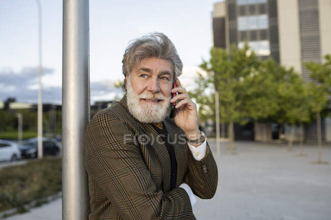 Uomo d'affari maturo appoggiato sul palo mentre parla attraverso il telefono cellulare in città — Foto stock