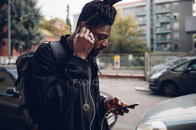Mann stellt In-Ear-Kopfhörer ein, während er Handy benutzt — Stockfoto
