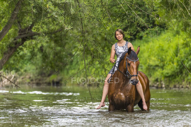 Young woman riding horse in river at forest — Stock Photo