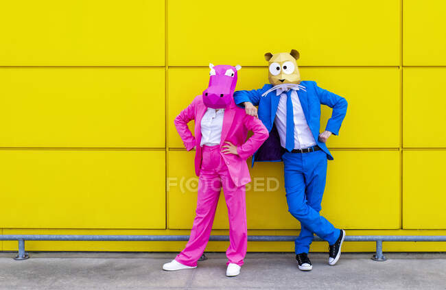 Man and woman wearing vibrant suits and animal masks posing together in front of yellow wall — Stock Photo