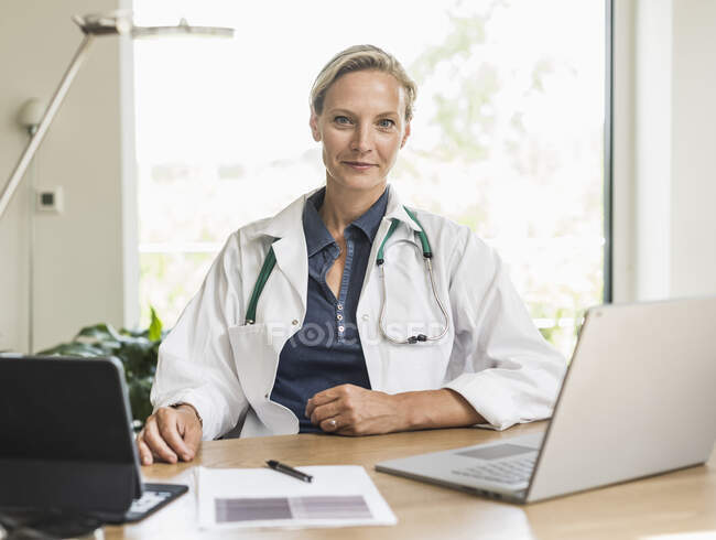 Medico femminile con laptop e tablet digitale seduto in ufficio — Foto stock