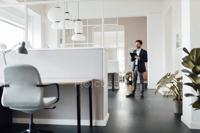 Homme d'affaires avec tablette numérique regardant loin tout en restant au bureau — Photo de stock
